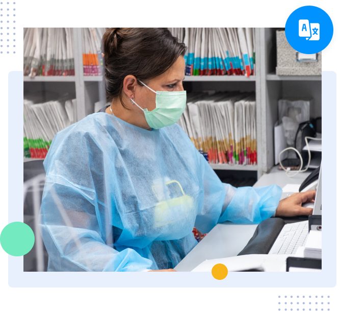 Medical worker in protective gown and mask checking patient records on a computer.